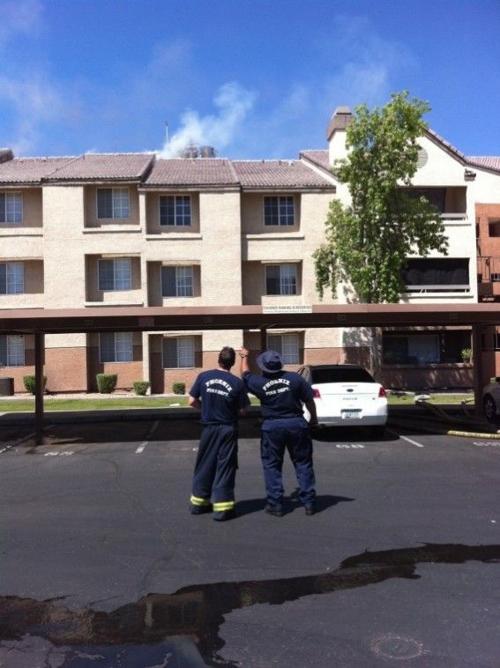 Two members of the Phoenix Fire Department look on as firefighters work on the roof.