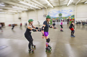 Reporter Skates After Her Derby Girl Dreams : With instruction from “Malice,” left, of the Port City Roller Girls roller derby team, slowly pushes News-Sentinel reporter Sara Jane Pohlman to teach her proper skating technique at the San Joaquin County Fairgrounds on Thursday, Feb. 7, 2013.
 - Photo by Dan Evans/News-Sentinel