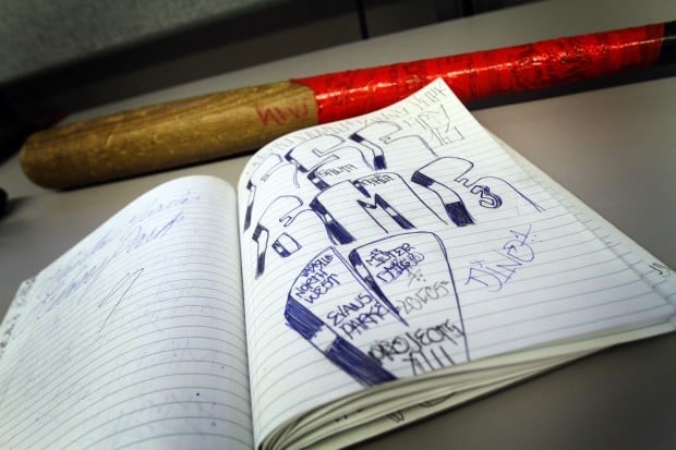 A baseball bat and a composition book with gang writing sits on the desk of