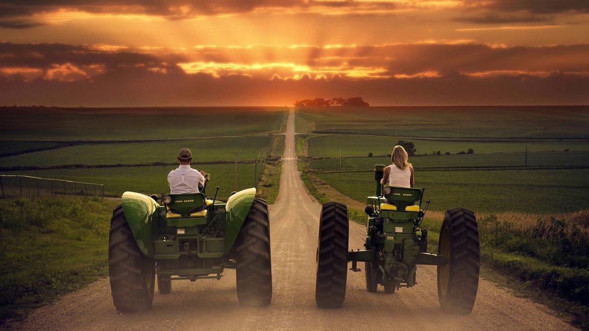 Farm couple riding down road on tractors