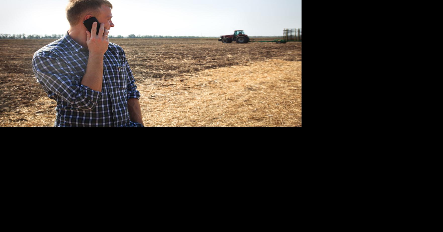 Young man with phone in a field and a tractor on a background.