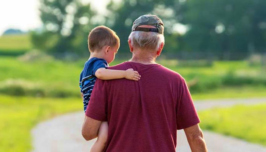 Older farmer carrying child in field