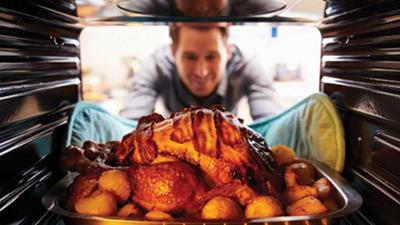 Man Taking Roast Turkey Out Of The Oven