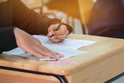 high school or university student hands taking exams, writing examination on paper answer sheet optical form of standardized test on desk doing final exam in classroom. Education literacy concept.