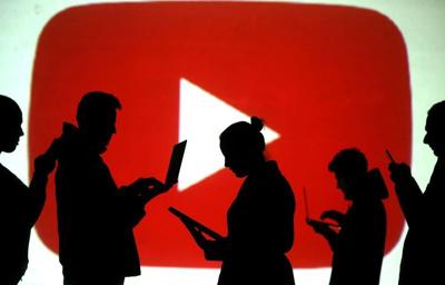 Silhouettes of laptop and mobile device users are seen next to a screen projection of Youtube logo in this picture illustration