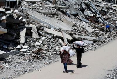 Palestinian woman and a girl carrying bags of firewood walk by the rubble of houses, in Gaza