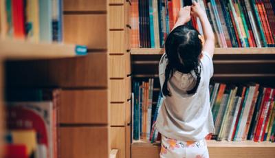Little Asian girl choosing books from the bookshelf in library