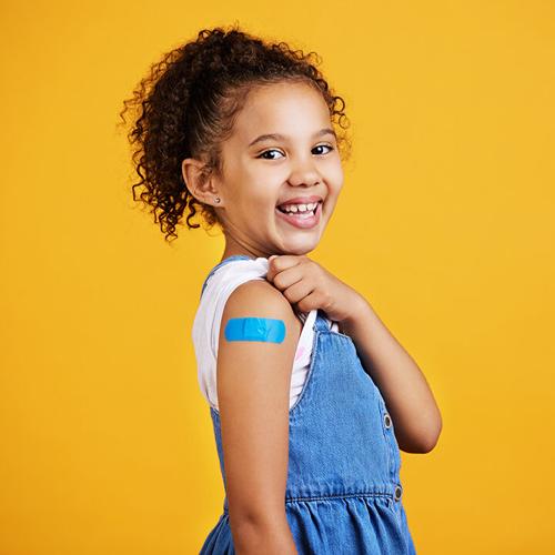 Happy, portrait and child with a plaster in a studio for a wound, sore or injury on her arm. Happiness, smile and healthy girl kid model posing with a bandaid after a vaccination by yellow background