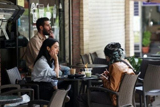 Two women sit at a cafe table with drinks in Tehran