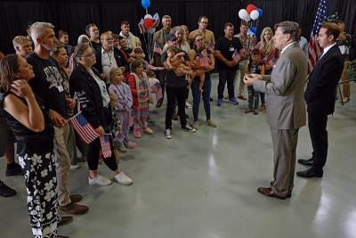 Newly arrived South Africans listen to U.S. Deputy Secretary of State Christopher Landau deliver welcome statements in a hangar near Washington Dulles International Airport on May 12, 2025.