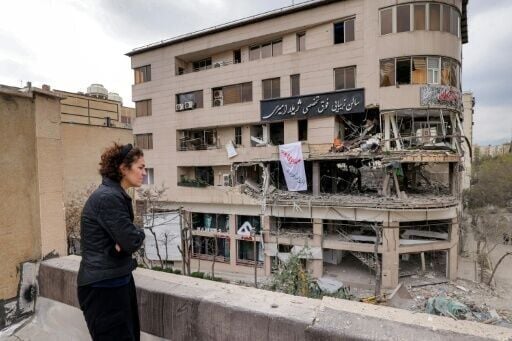 A woman standing on a rooftop in Tehran views destruction in an office building that housed the offices of the Doha-headquartered news network Al Araby TV following a missile strike on March 29, 2026