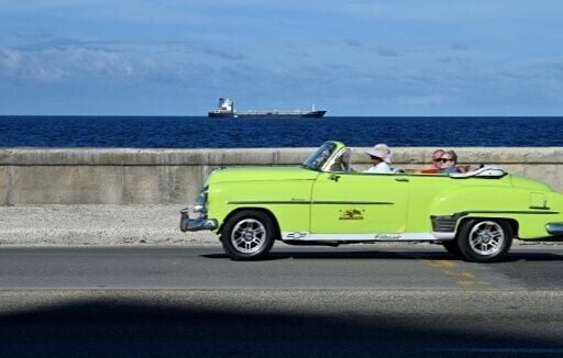An ageing American car drives along the ocean front in Havana as an oil tanker arrives in the Cuban capital