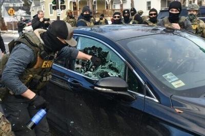 A federal officer breaks a car window to begin the process of removing a woman from her vehicle near the area of an ICE operation in Minneapolis, Minnesota