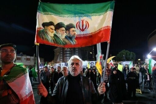 A man carries an Iranian flag with the portraits of Iran's late supreme leader, Ayatollah Ruhollah Khomeini (L), slain supreme leader Ayatollah Ali Khamenei (C) and Iran's supreme leader Ayatollah Mojtaba Khamenei as people rally in his support