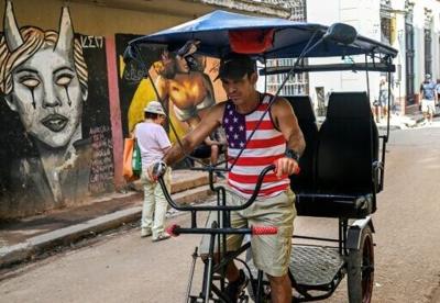 A man wearing a US-flag designed T-shirt rides his tricycle along a street in Havana
