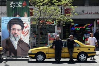 A taxi stands next to a banner depicting Iran's new supreme leader Ayatollah Mojtaba Khamenei, along a street in Tehran