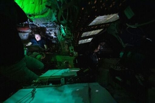 This handout picture by an Artemis II crew member provided by NASA shows Christina Koch illuminated by a screen inside the darkened Orion spacecraft as Jeremy Hansen (R) peers out of one of Orion's windows