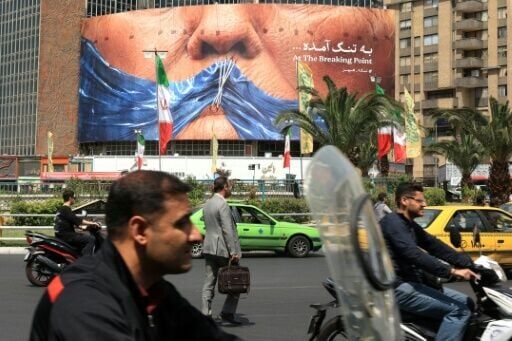 Commuters make their way past an anti-US billboard referring to President Donald Trump and the Strait of Hormuz, installed on a building in Tehran