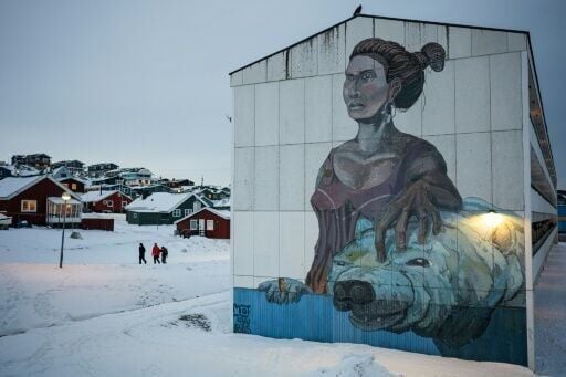 People walk past a large mural depicting a woman and a polar bear on the side of a building in Greenland's capital