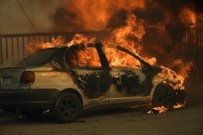 A vehicle and a house are engulfed in flames during a wildfire in Concepcion, Chile, on January 18, 2026