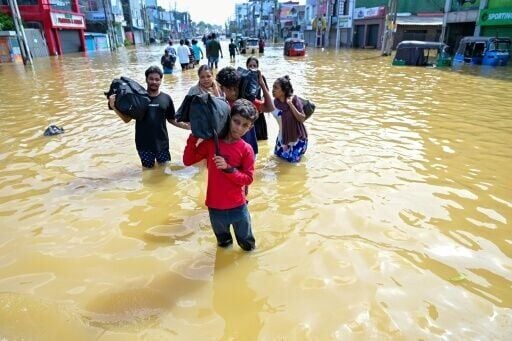 People wade through a flooded street on the outskirts of Colombo on November 30