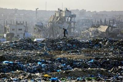 A Palestinian boy searches for recyclable material at a landfill against the backdrop of destroyed buildings in Khan Yunis, in the southern Gaza Strip