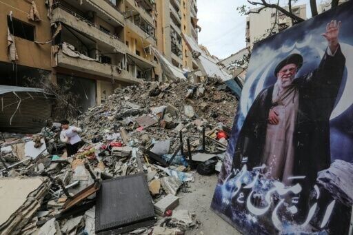 A boy stands amid the debris of a destroyed building next to a portrait of Iran's slain supreme leader Ayatollah Ali Khamenei