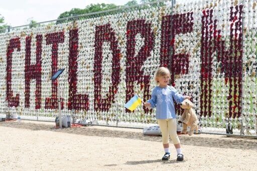 A 4-year-old Ukrainian girl waves a Ukrainian flag as she stands alongside a fence featuring 20,000 stuffed teddy bears installed meant to represent Ukrainian children displaced by Russia in the war