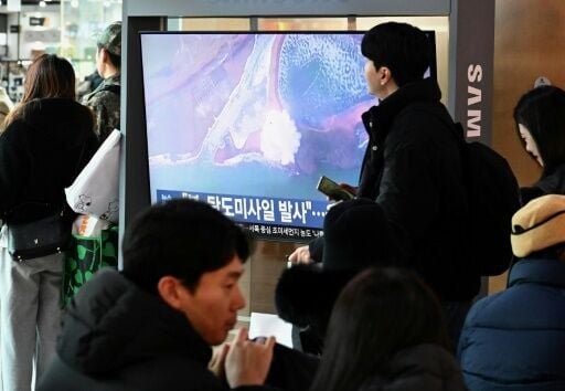 People in front of a TV screen showing footage of a North Korean missile test, at a train station in Seoul