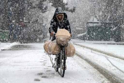 An Afghan man rides a bicycle along a road during snowfall in the green zone area of Kabul on January 22, 2026.