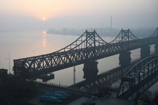 The sun rises over the North Korean town of Sinuiju, behind the Sino-Korean Friendship Bridge (L) and the Yalu River Broken Bridge (R), as seen from the border city of Dandong, in China's northeast Liaoning province on March 26, 2026.