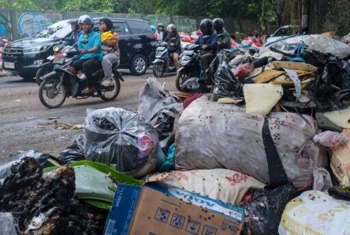 Vehicles driving along a road littered with illegally dumped waste in Pamulang, South Tangerang, Banten