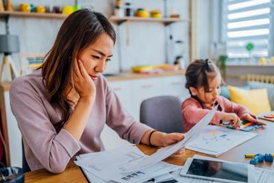 Young stressed mother checking her finances while her daughter is playing next to her