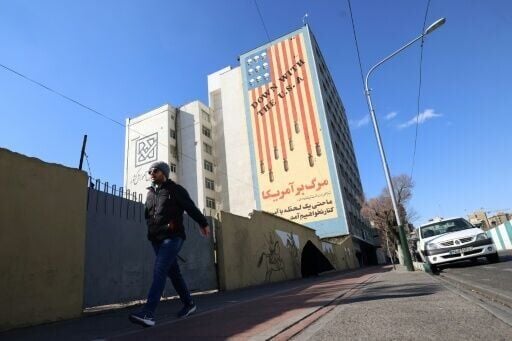 A man walks past a large anti-US mural on the side of a Tehran building