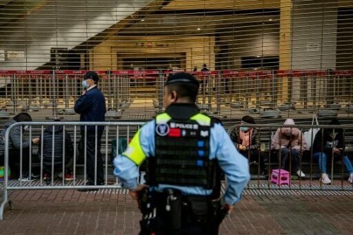 A police officer keeps watch as people wait in line to enter the West Kowloon Law Courts building