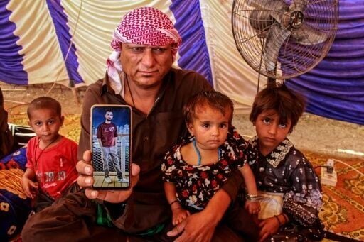 Abdul Malick (2L), a transporter and uncle of Pakistani national Muzaffar Ali, who was killed in Dubai amid the ongoing Middle East war, displays a photograph of Ali on his mobile after his funeral in Jamshoro, in Sindh province on March 12, 2026