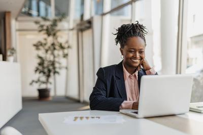 A smiling businesswoman works at her laptop, illustrating a joyful and productive mood in a stylish modern office setting featuring natural lighting and contemporary design.