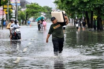 A hotel guest carries his suitcase as he wades through the water on an inundated street amid floods following heavy rain at Legian Kuta near Denpasar