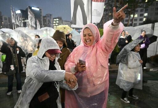 BTS fans react as they watch a live concert by K-pop boy band BTS on their mobile phones outside a stadium where the group is performing in Goyang on April 9, 2026.