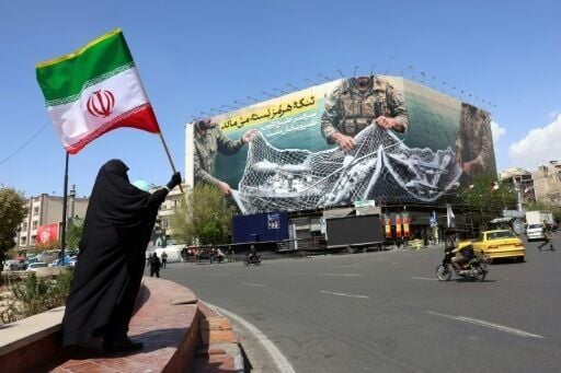 A woman holds Iran's national flag while standing near a billboard reading 'The Strait of Hormuz remains closed' at Enqelab Square in Tehran on April 5, 2026