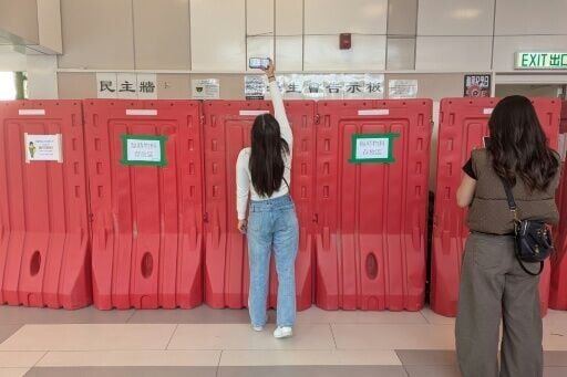 A woman takes a photo with her phone above barricades in front of the student union-run notice board, nicknamed “democracy wall”, at Hong Kong Baptist University