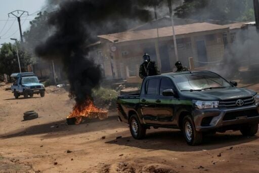 Guinea Bissau security forces patrol cars drive near burning tyres