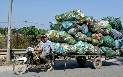 Men on a motorbike pull a cart carrying plastic waste on the outskirts of Hanoi