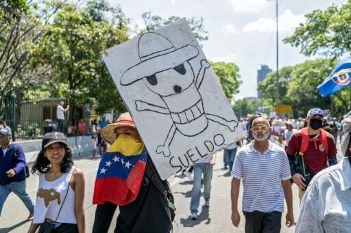 A Venezuelan demonstrator holds a sign featuring a skull and reading 'wage' at a protest against what many refer to as 'starvation' wages