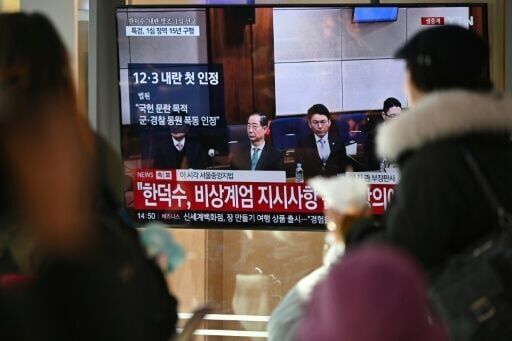 People watch a television screen showing a live broadcast of the trial verdict of South Korea's former prime minister Han Duck-soo (L on the screen) on charges related to martial law, at a train station in Seoul on January 21, 2026