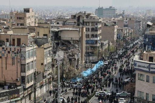 Iranians walk past a damaged building in Tehran