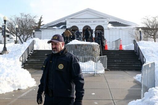 A police officer looks on as members of the media gather outside the site of Hillary Clinton's deposition