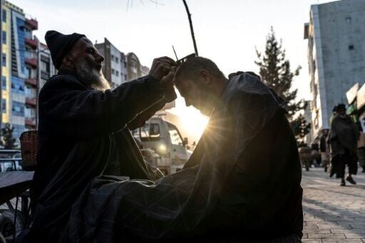 An Afghan barber trims a customer's hair along a sidewalk in Kabul