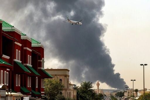 An Emirates aircraft prepares for landing as a smoke plume rises from an ongoing fire near Dubai International Airport in Dubai on March 16, 2026