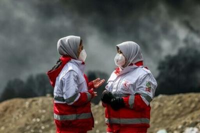 Members of Iranian Red Crescent Society standing near smoke plumes. The IFRC launched an emergency appeal to help support the IRCS's crisis response